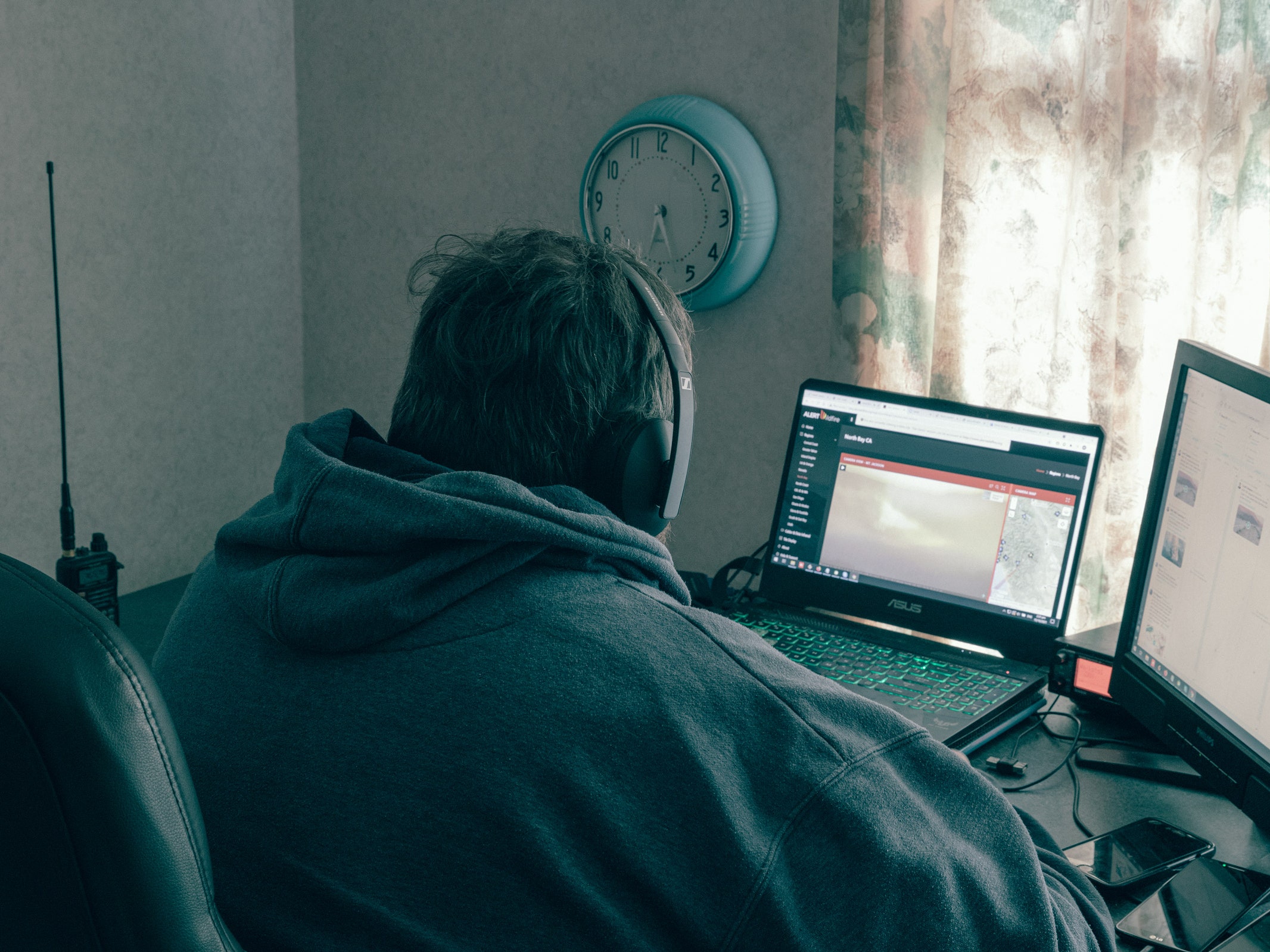 Back of Mike Silvester at his desk looking at two computer monitors with four phones on his desk and a scanner to his side