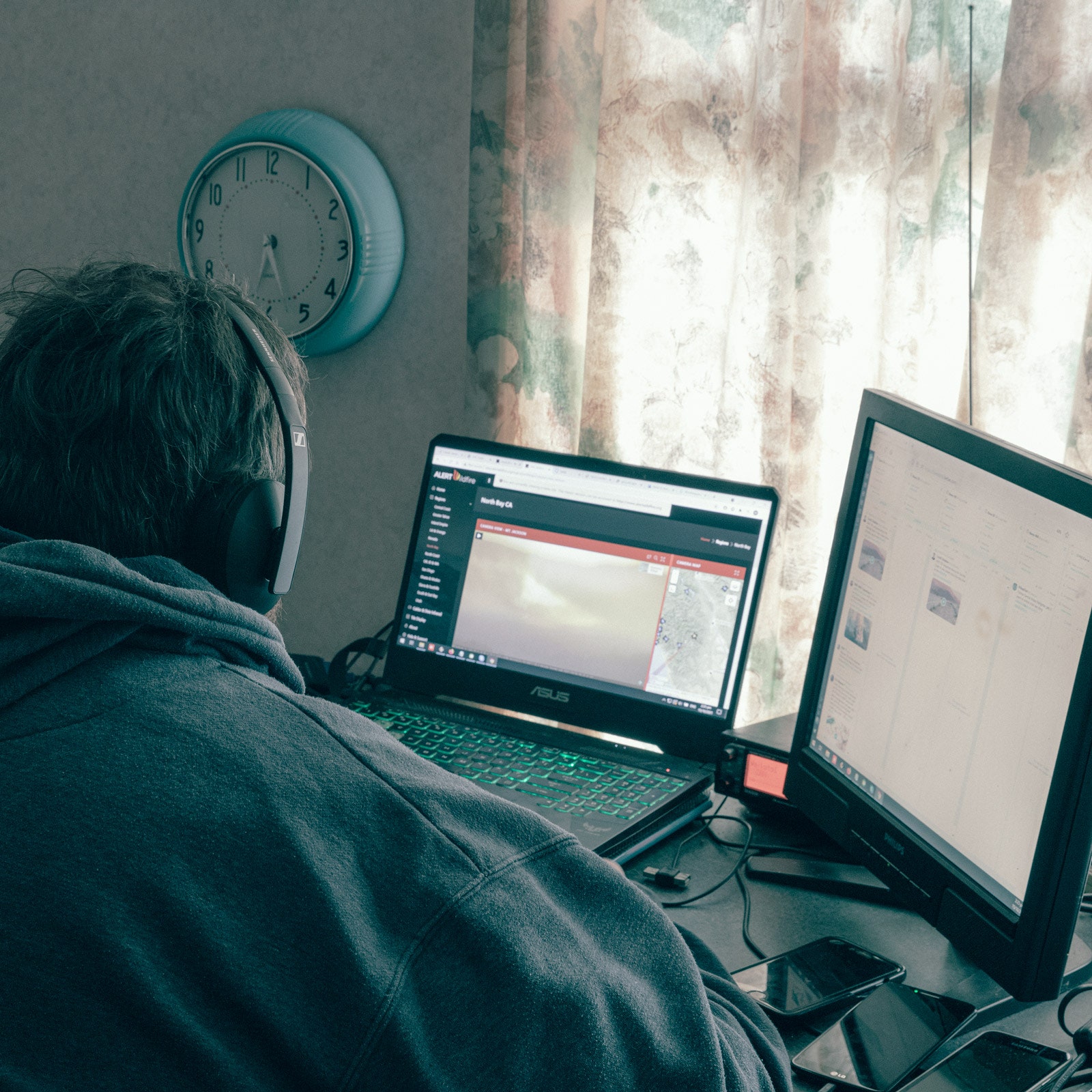 Back of Mike Silvester at his desk looking at two computer monitors with four phones on his desk and a scanner to his side