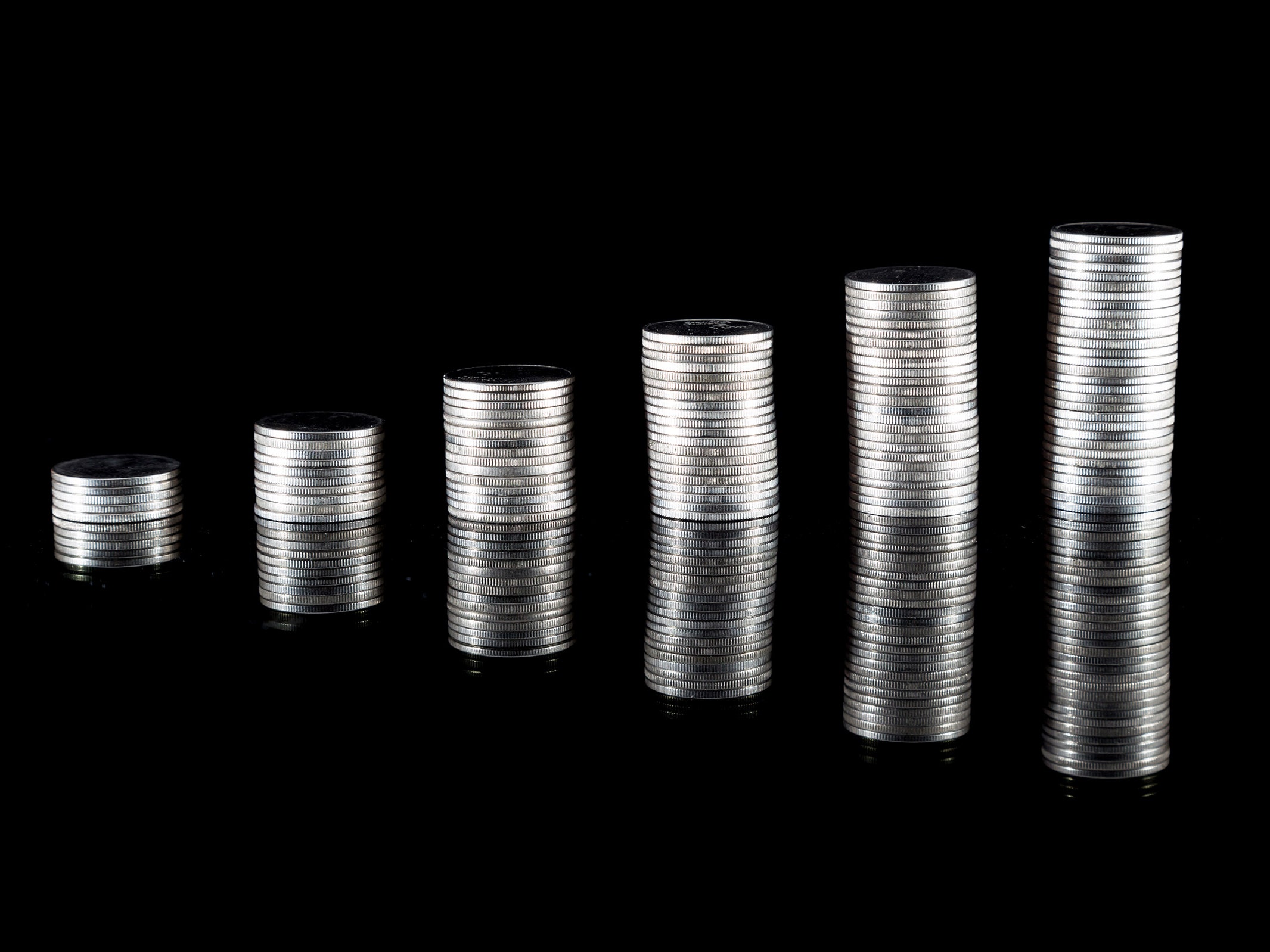 Stacks of coins next to each other increasing in height on a black background