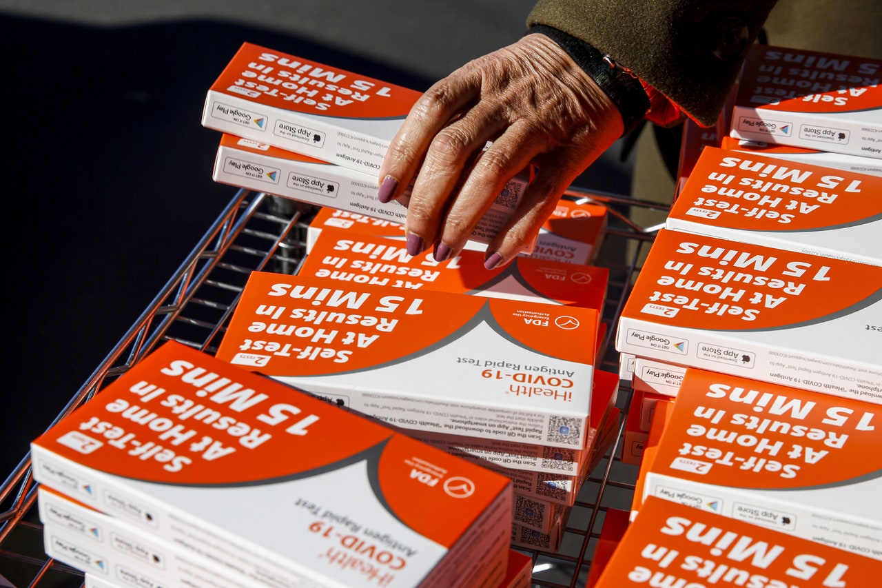 Hand reaching into box full of boxes of Covid19 rapid tests