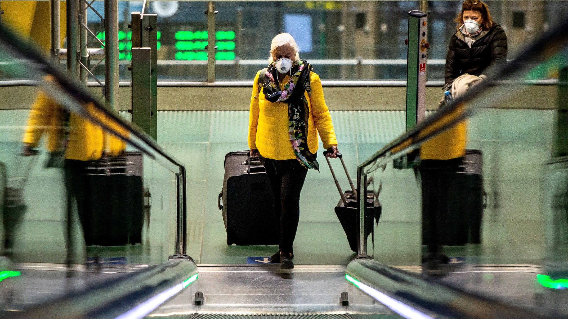 Woman walking up escalator with suitcases at airport